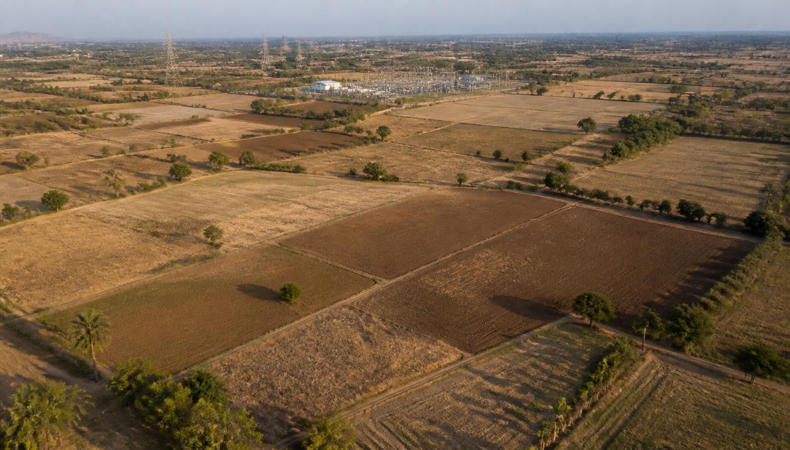 Aerial view of farmland parcels with a substation and transmission lines on the horizon